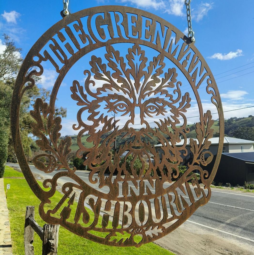 The Greenman Inn sign, a foliate Green Man cut from weathered steel, with the Adelaide Hills behind